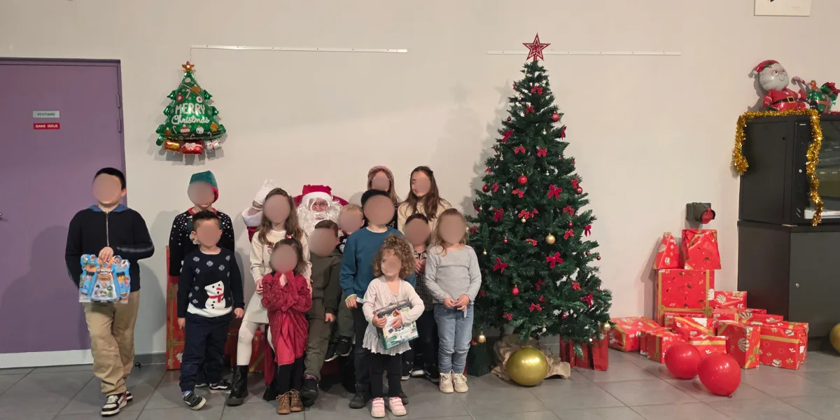 Groupe de personnes posant devant un grand sapin de Noël, entouré de cadeaux rouges, visages floutés